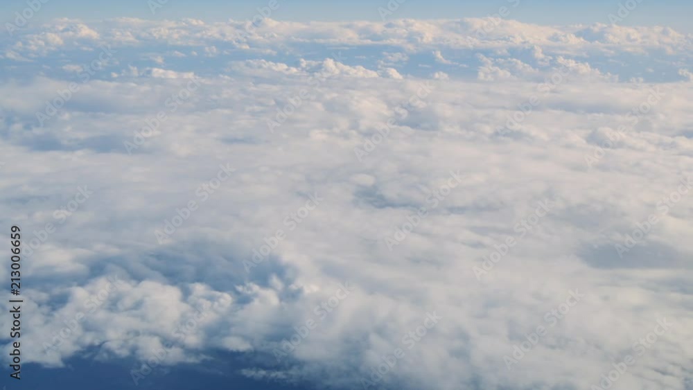View from plane travelling high over white clouds with ocean below and distant horizon View from plane travelling high over white clouds with ocean below and distant horizon