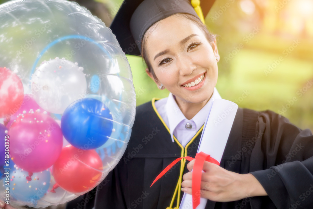 Fototapeta premium Graduate woman students wearing graduation hat and gown in the garden 