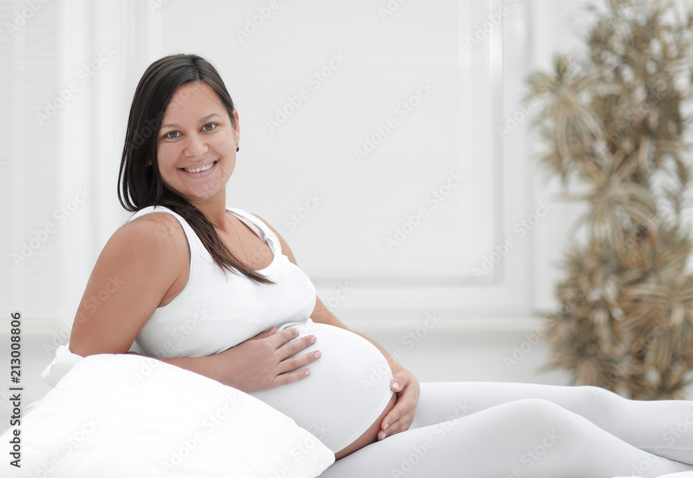 Beautiful pregnant woman sitting at sofa and keeping hand on belly. Beautiful pregnant woman sitting at sofa and keeping hand on belly.