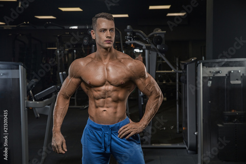 A young handsome sexy male athlete bodybuilder posing in front of a camera on a dark background in a modern sports hall. Concept healthy way of life, proper nutrition, coaching. Personal trainer.