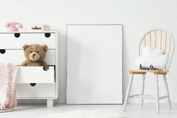 Mockup of empty poster and cabinet with plush toy and pink blanket in white child's room interior. Real photo