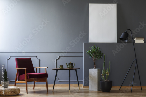 Red armchair next to table in grey apartment interior with mockup and copy space. Real photo