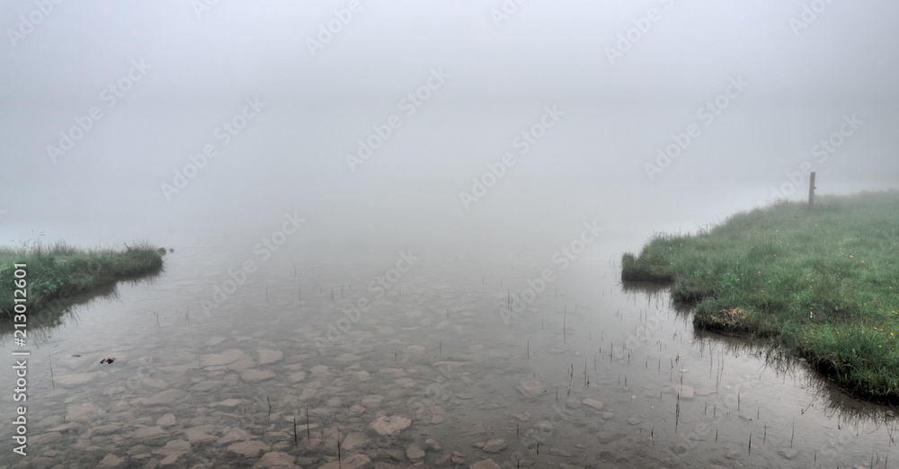 mountain lake and shore in thick fog