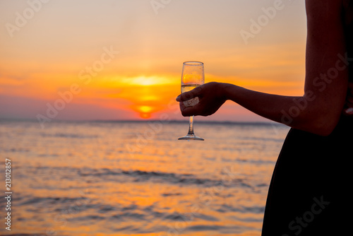 woman at sunset. Elegant girl is drinking champagne at sunset. Girl with glass on background setting sun. romantic date in the evening. Luxury woman drinking from a wine glass on the beach. 