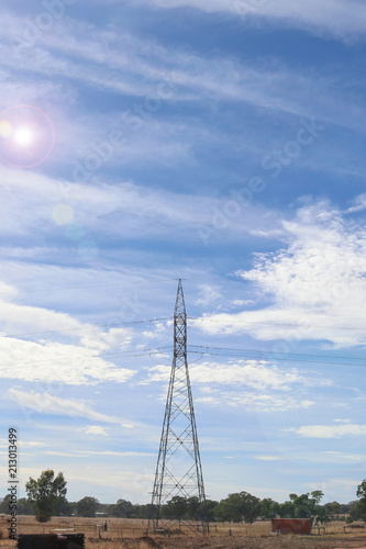 a power line support tower in a blue cloudy sky with lens flare