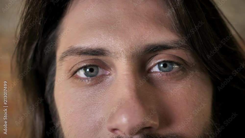 Eyes of young nice brunette man with beard is watching at camera, brick background Eyes of young nice brunette man with beard is watching at camera, brick background