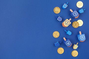 Dark blue background with multicolor dreidels and chocolate coins. Hanukkah and judaic holiday concept.