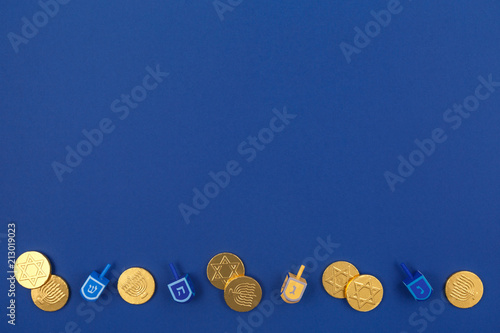 Dark blue background with multicolor dreidels and chocolate coins. Hanukkah and judaic holiday concept.