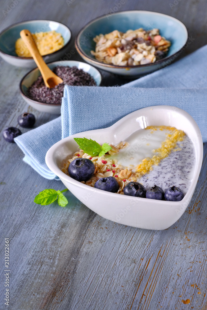 Yogurt with muesli, blueberries, poppy seeds, mint and crushed cornflakes served in heart-shaped bowl