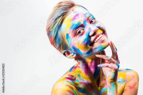 smiling attractive girl with colorful bright body art touching chin isolated on white