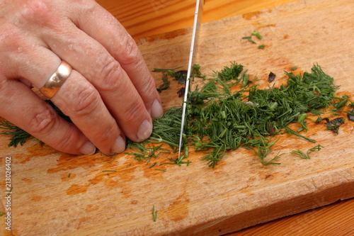 Female hands chopping the dill leaves on a cutting board with a knife
