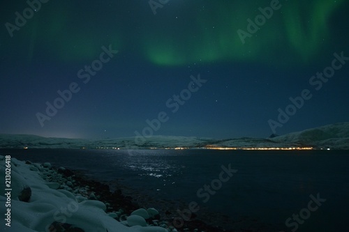The northern lights (Aurora Borealis) over Seljelvnes, Troms by the sea and the snowy mountains © BAHADIRARAL
