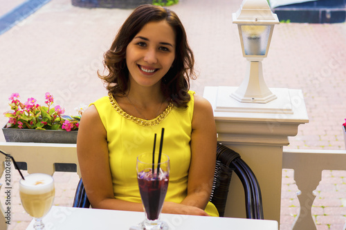 Beautiful girl in bright yellow dress sitting in summer Cafe