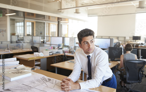 Young male architect leaning on desk in open plan office