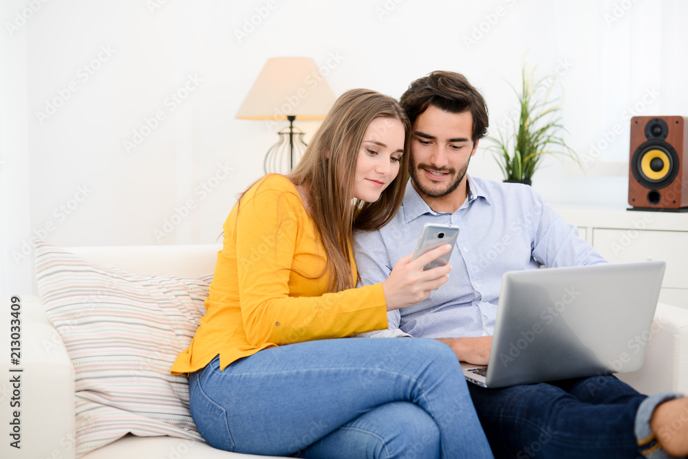 cheerful young couple on sofa at home websurfing and shopping online with laptop computer internet technology