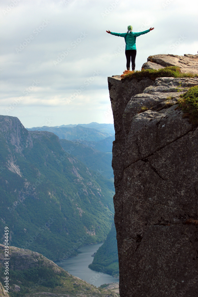 Woman stands on a cliff spreading her arms at Preikestolen rock (Preacher's Pulpit) over Lysefjord, Norway
