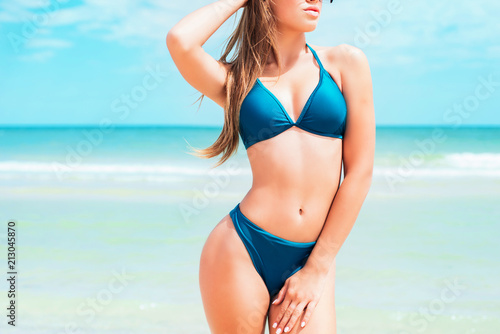 A beautiful young girl with long hair in a blue swimsuit  relax on beach in the sea in sunny hot day