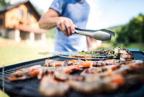 Billede på lærred Unrecognizable man cooking seafood on a barbecue grill in the backyard