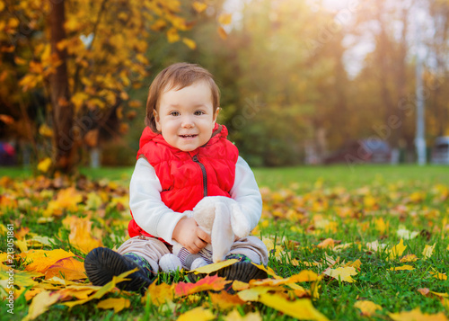happy little girl 3 years old sitting surrounded by yellow fallen leaves