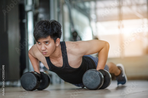 Sport. Handsome man doing push ups exercise with one hand in fitness gym.Fitness instructor at the gym - Control your mind, conquer your body.Handsome muscular man is working out with dumbbells in gym © Day Of Victory Stu.