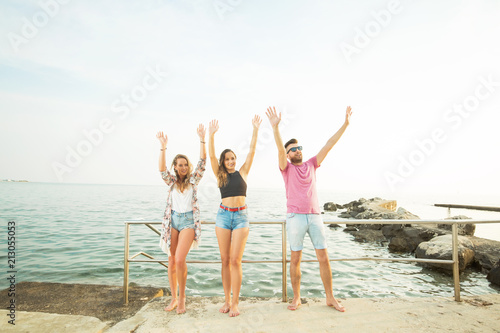 Three happy friends standing on a sea shore in front of a camera