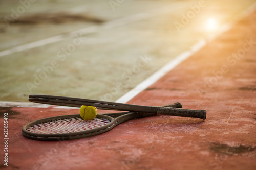 Tennis ball and racket on hard court under sunlight