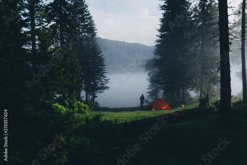 Foggy morning in the forest, rays of light illuminate the camping tent, overlooking the lake © Pavel