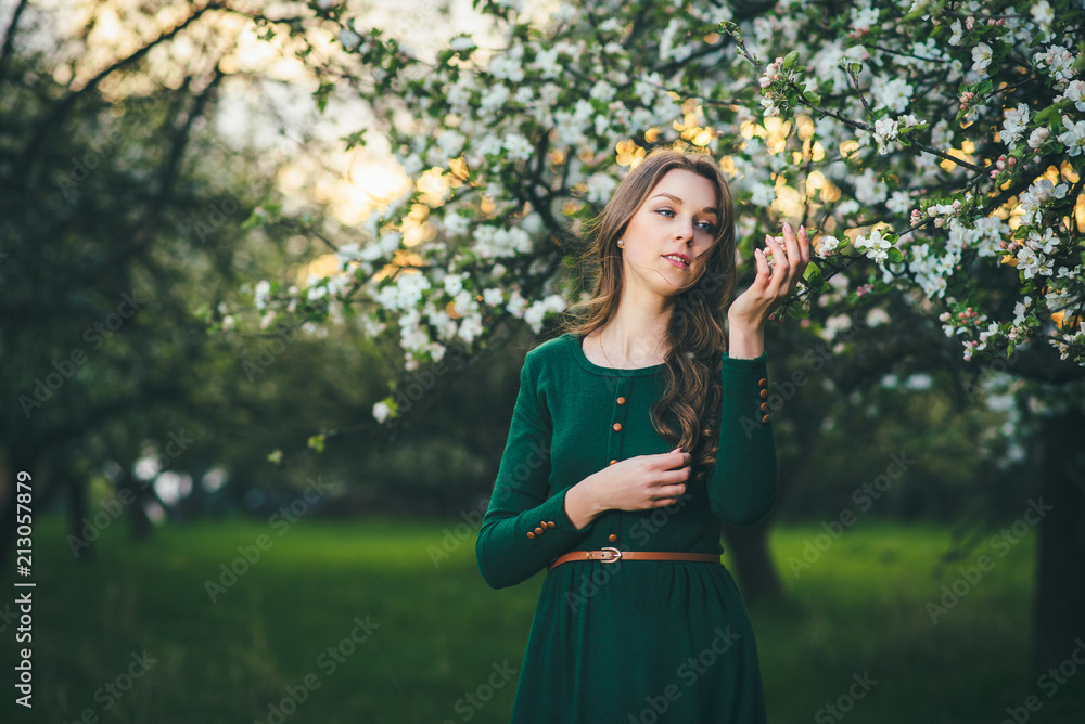 Young beautiful woman in green dress posing in the blooming garden at the sunset Young beautiful woman in green dress posing in the blooming garden at the sunset