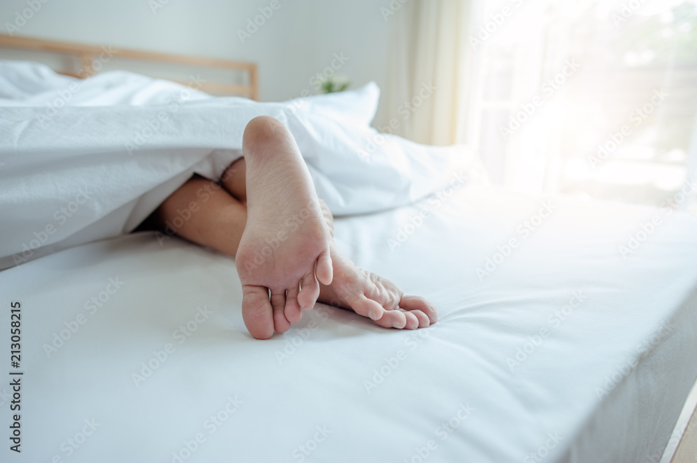 Young female sleeping in bed at home with focus on legs. Feet of woman