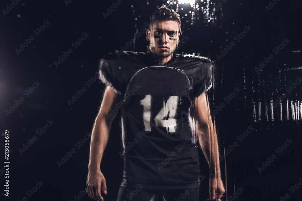 view of young american football player looking at camera on black through wet glass view of young american football player looking at camera on black through wet glass