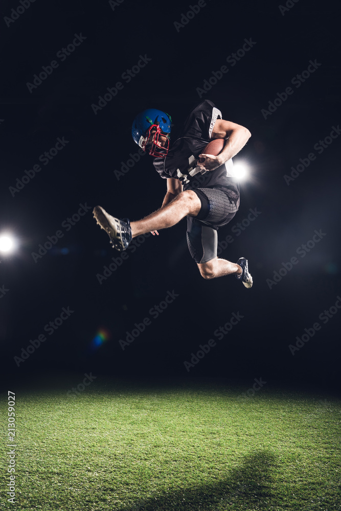 american football player jumping with ball over green grass on black