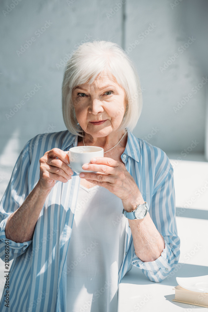 portrait of grey hair woman with cup of coffee standing at windowsill at home portrait of grey hair woman with cup of coffee standing at windowsill at home