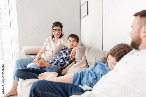 Photo of happy family with two children resting in living room at home, and sitting on sofa together