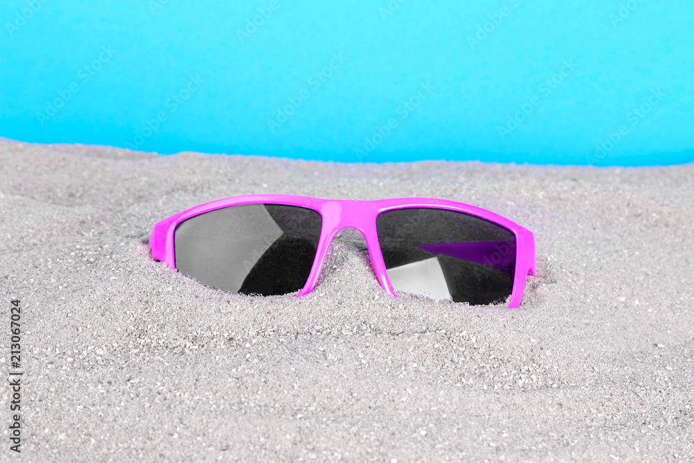 pink sunglasses in the sand close-up on a blue background