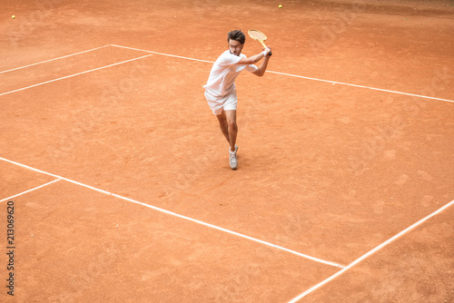 old-fashioned tennis player training with wooden racket on brown court