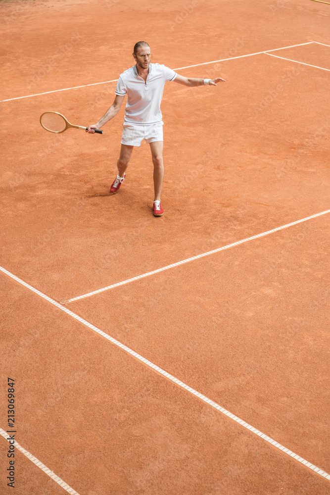 old-fashioned tennis player training with retro wooden racket on brown court