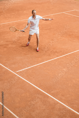 old-fashioned tennis player training with retro wooden racket on brown court