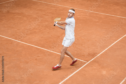 retro styled man in white sportswear playing tennis with wooden racket on court