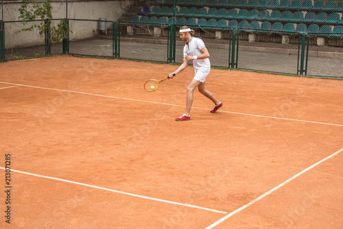 retro styled man in white sportswear playing tennis with racket and ball on court