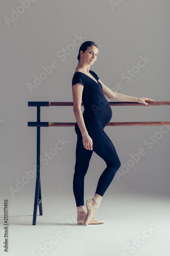 Young beautiful pregnant ballerina is posing in studio