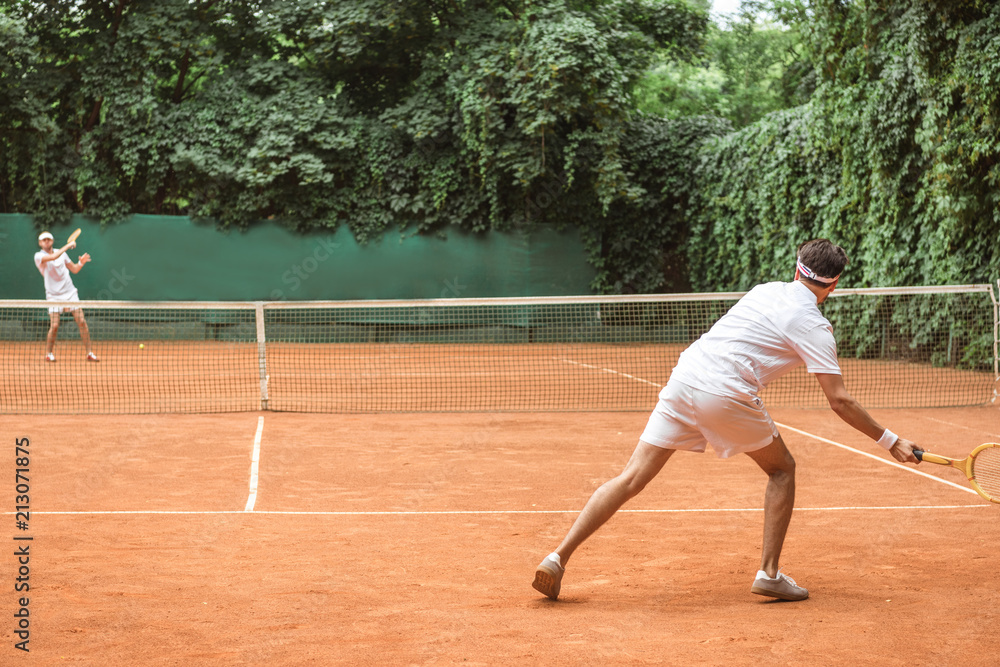 old-fashioned sportsmen playing tennis with wooden rackets on court
