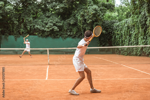 sportsmen in white sportswear playing tennis with wooden rackets on court
