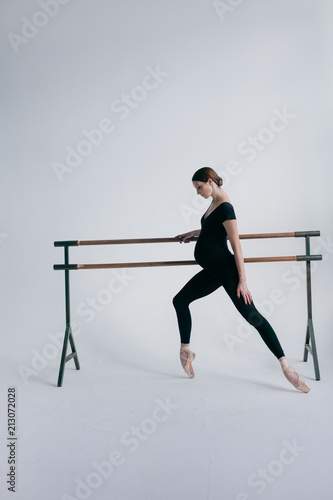 Young beautiful pregnant ballerina is posing in studio
