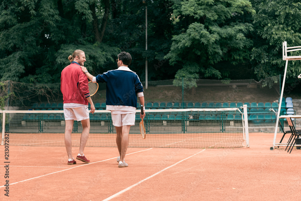 rear view of old-fashioned friends with wooden rackets walking on tennis court