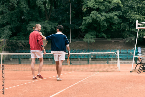 rear view of old-fashioned friends with wooden rackets walking on tennis court
