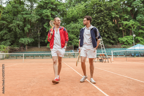 retro styled friends with wooden rackets walking on tennis court