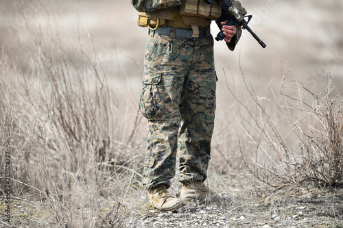 Automatic rifle detail and military camouflage uniform on a soldier in a field