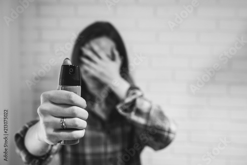 Married woman is holding pepper spray canister for personal protection. Girl covers her face with hands. White background behind. Self-defense photo. Copy space place.