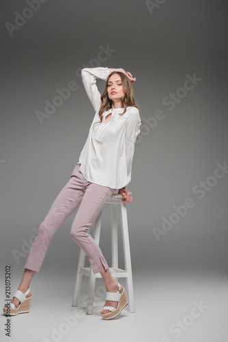 beautiful woman sitting on chair and looking at camera on grey background