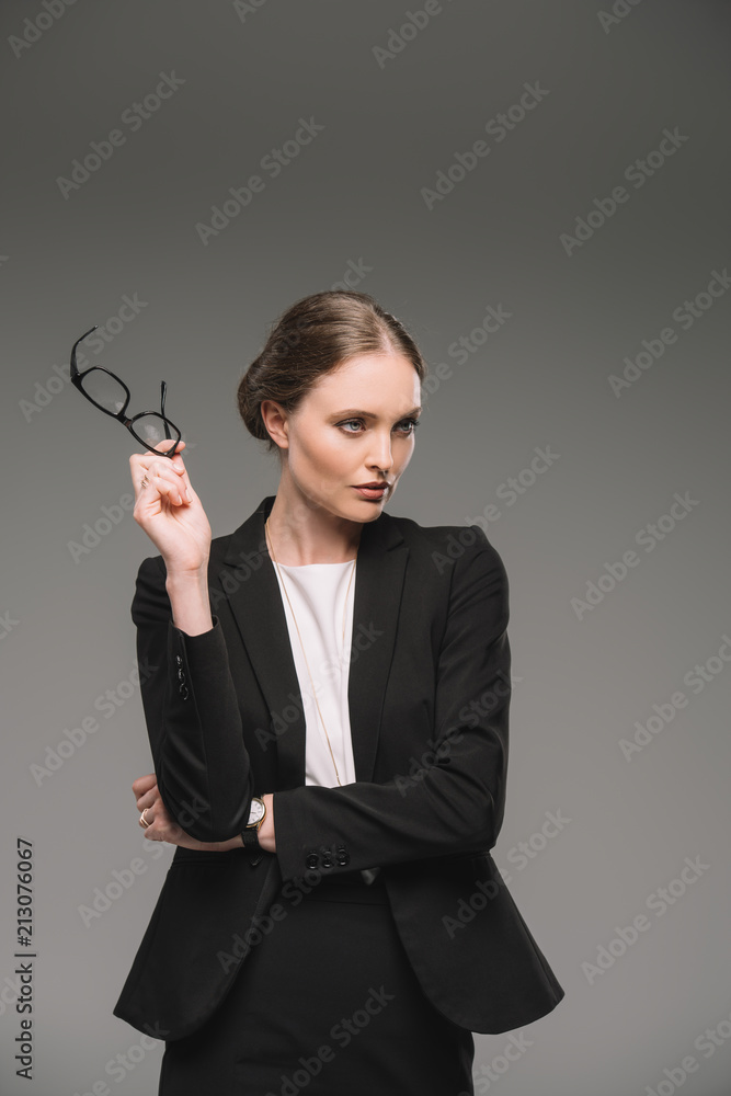beautiful businesswoman holding eyeglasses and looking away isolated on grey background beautiful businesswoman holding eyeglasses and looking away isolated on grey background